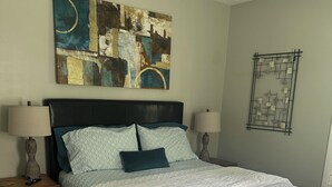 A bedroom with a large bed, two bedside tables, a wall art piece, and a decorative wall hanging.