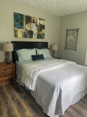 A bedroom with a large bed, two bedside tables, a wall art piece, and a decorative wall hanging.