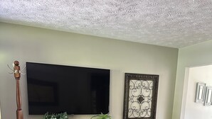 A living room with a wooden cabinet, a flat-screen TV, decorative wall art, and a floor lamp.