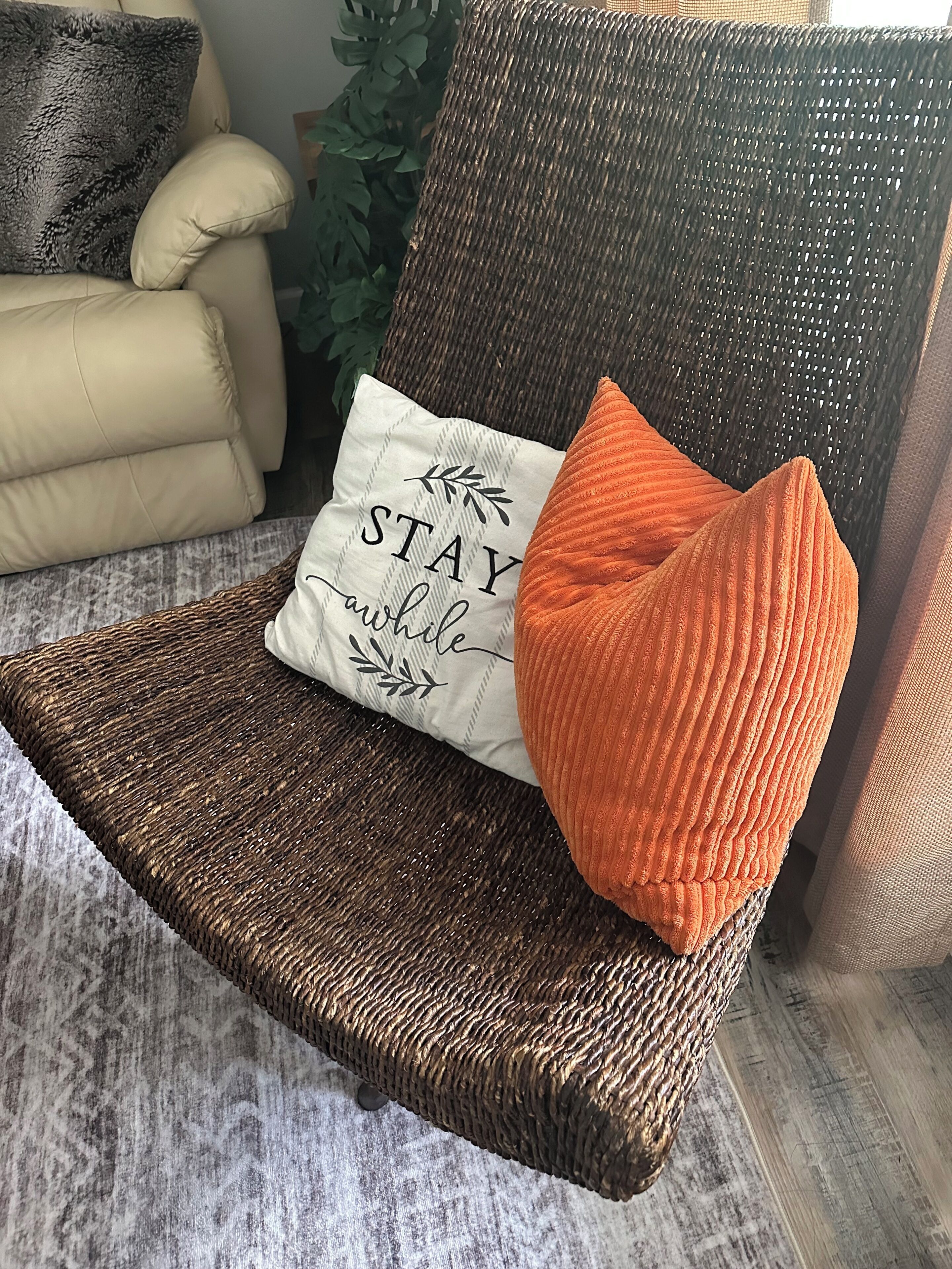 A wicker chair with a cushion and a pillow with text.
