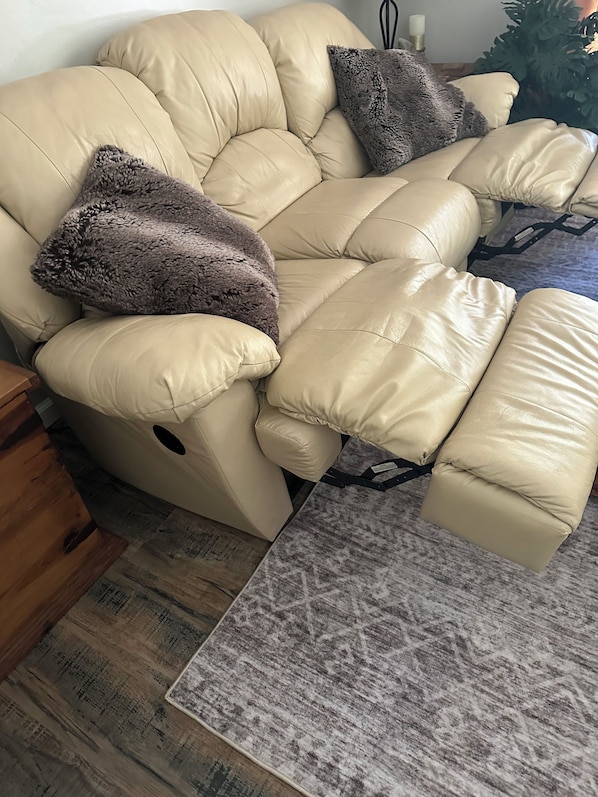 A beige leather sofa with multiple cushions, a patterned rug, and a wooden floor.