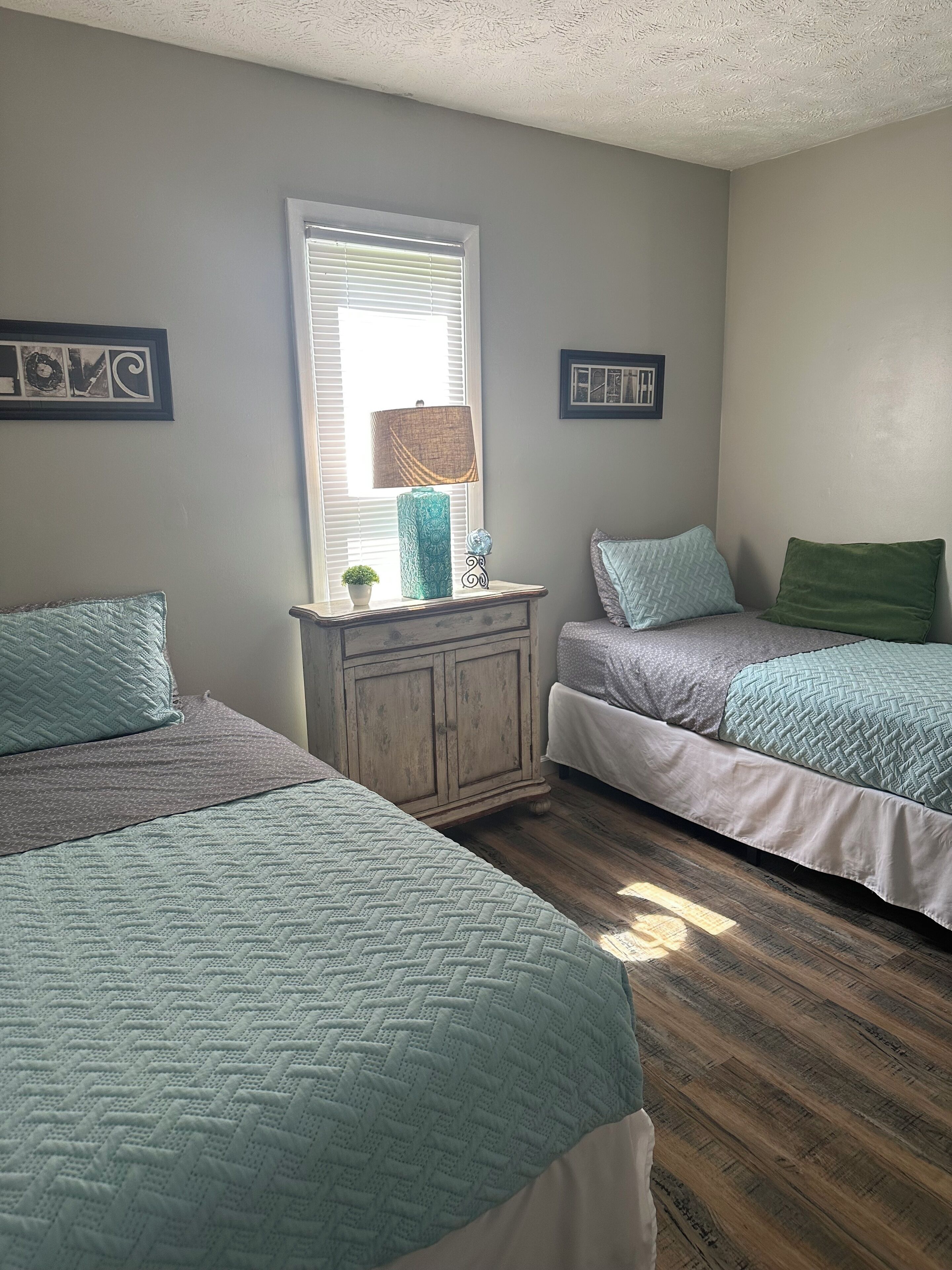 Een slaapkamer met twee bedden, een dressoir en een raam met jaloezieën.