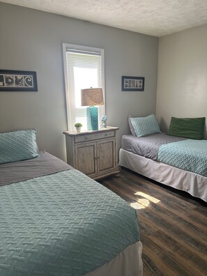 A bedroom with two beds, a dresser, and a window with blinds.
