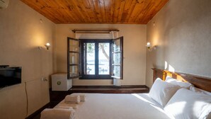 Un dormitorio con techo de madera, una cama con ropa de cama blanca, una ventana con cortinas y un televisor en la pared.