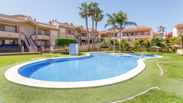 A swimming pool surrounded by a well-maintained lawn, with a multi-story building in the background. - 'Nomad House' Apartment with Shared Pool, Wi-Fi, and Air Conditioning (Gran Alacant)