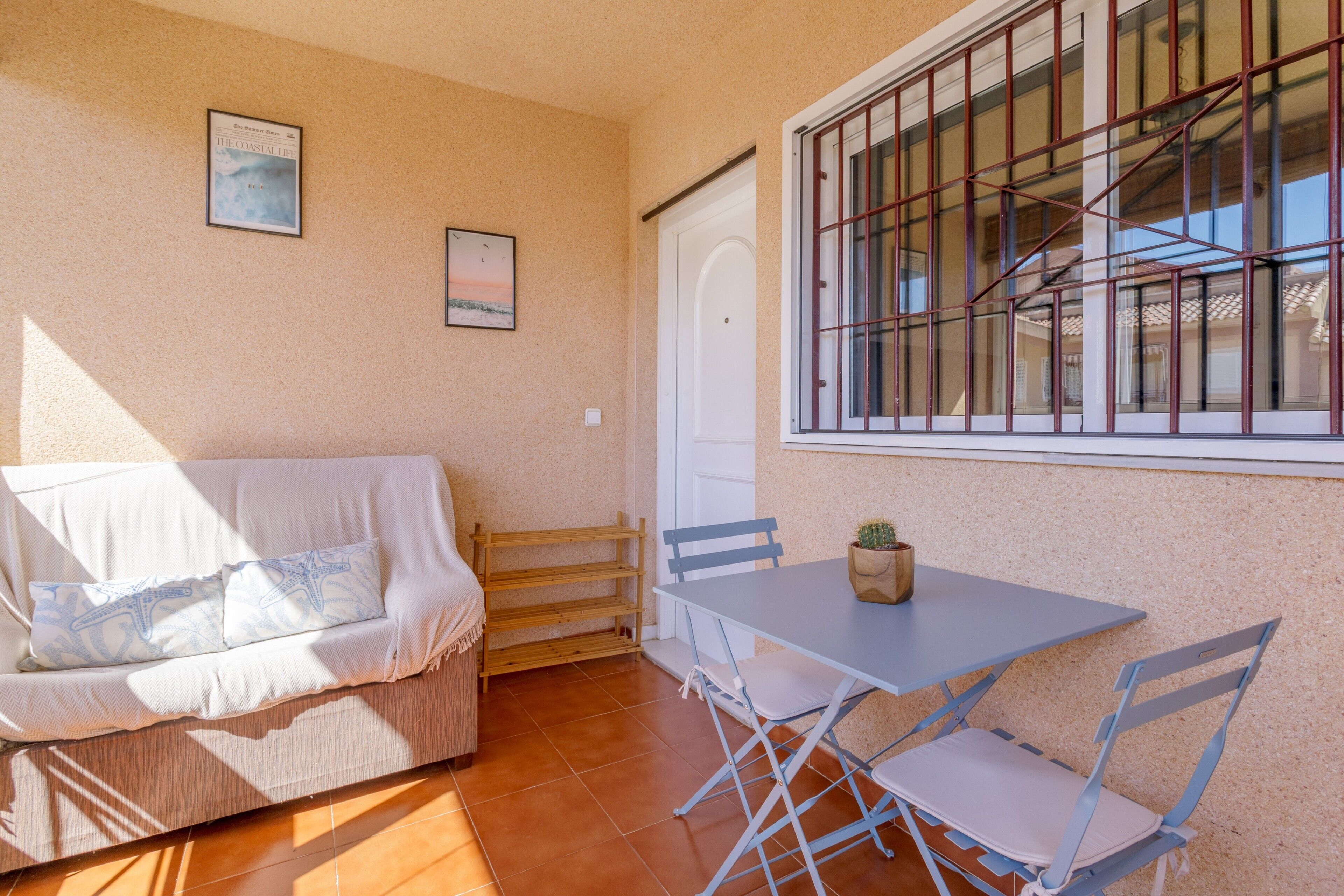 Ein Zimmer mit einer Couch, einem Tisch mit Stühlen, einem Fenster mit Gitterstäben und einer Tür.