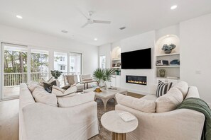 A modern living room with a sofa set, a coffee table, a flat-screen TV, a fireplace, and a balcony with a view of trees. - The Seagrove Escape|Easy Beach Access|Private Pool|Golf Cart (Santa Rosa Beach)