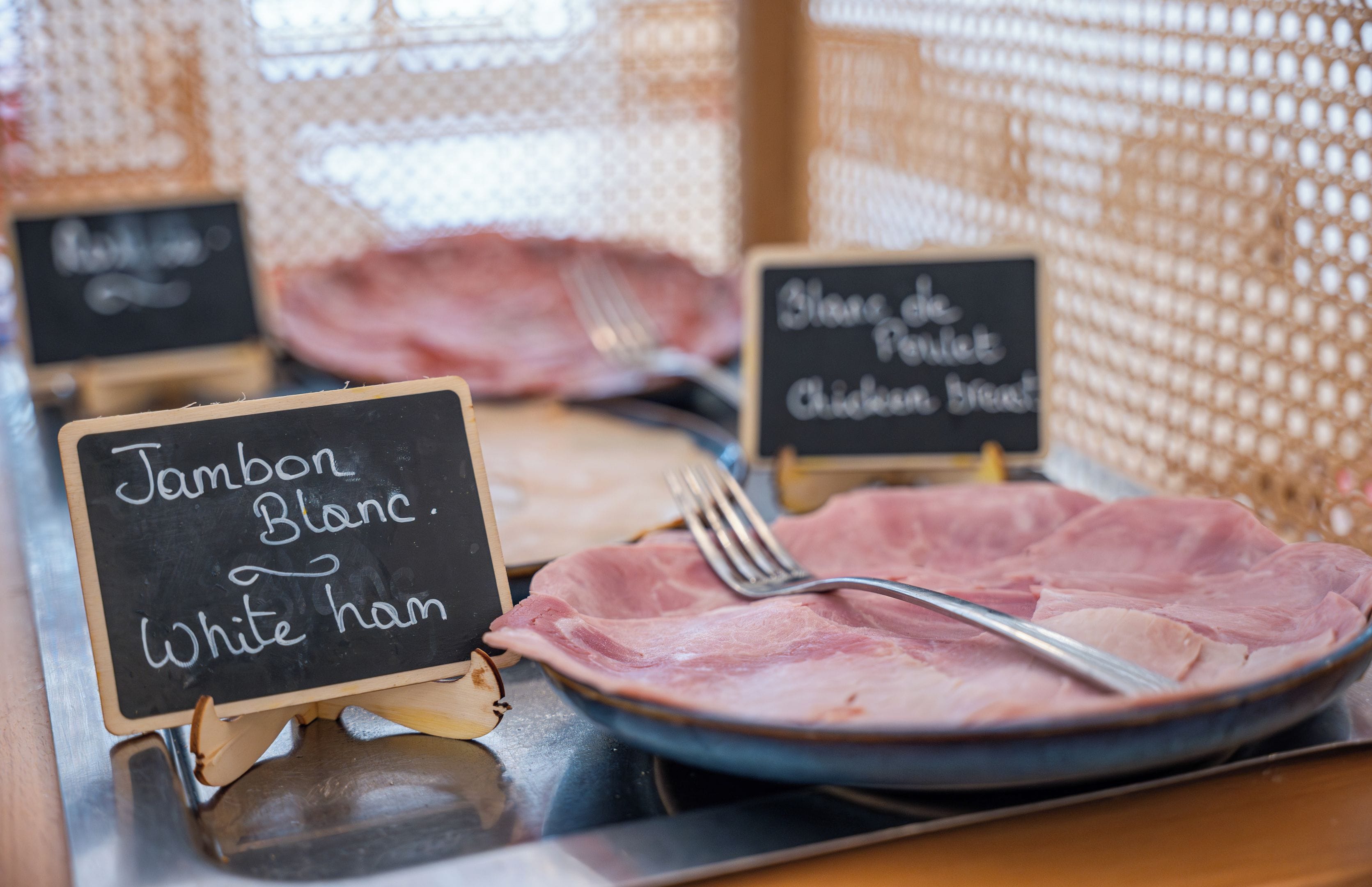 A menu board with 'Jambon Blanc' and 'White ham' options, a fork on a plate, and a chalkboard sign in the background.
