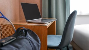 Ein Laptop auf einem Holztisch, ein Stuhl und ein Tennisschläger, der an der Wand lehnt.