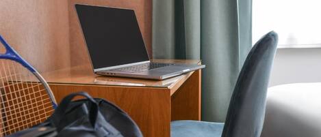 A laptop on a wooden desk, a chair, and a tennis racket leaning against the wall.