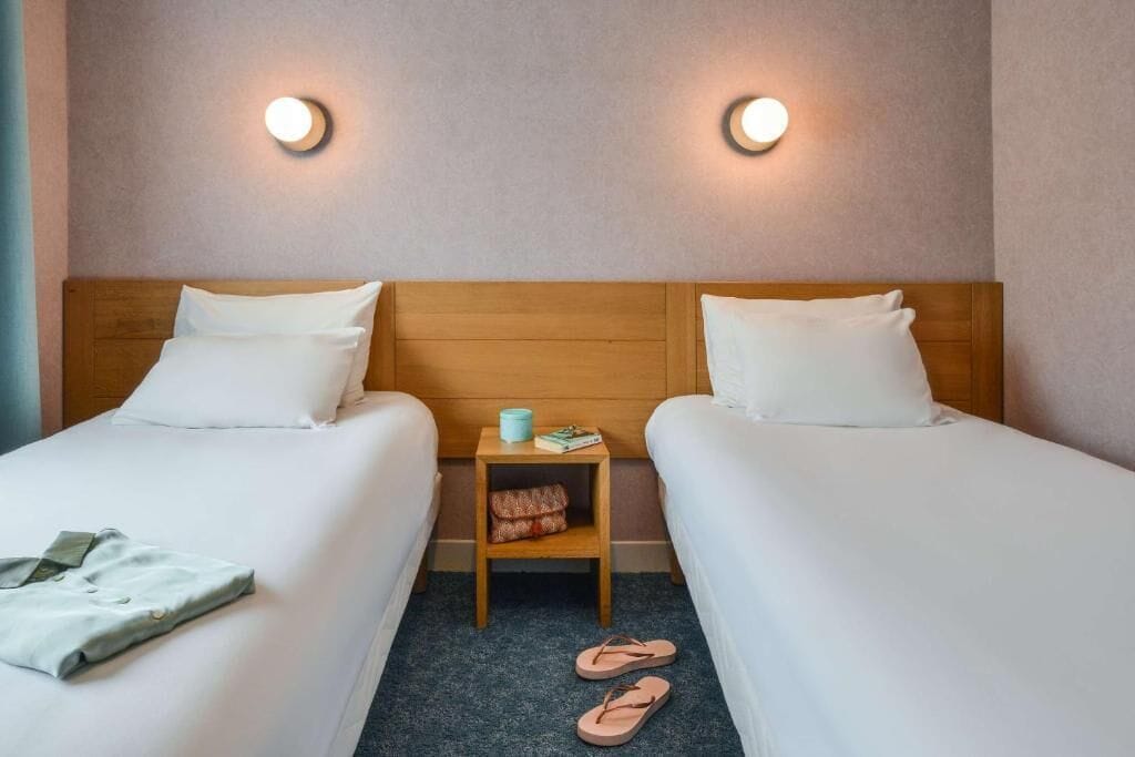 A hotel room with two beds, a nightstand, and two wall-mounted lights.