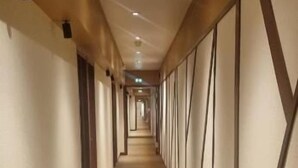 Ein langer, schmaler Hotelgang mit einem gemusterten Teppich, Holzvertäfelung an den Wänden und eingelassener Beleuchtung.