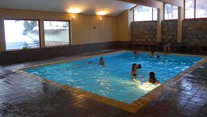 Une piscine intérieure aux murs en pierre, dotée de grandes fenêtres et d’un sol carrelé.