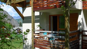 Un balcon en bois avec une table et des chaises, une fenêtre et une vue sur une montagne.