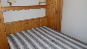 Un lit en bois avec une couvre-lit à motifs, deux lampes fixées au mur et une tête de lit en bois ornée d’un motif festonné.