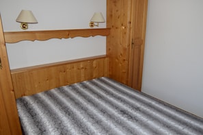 Ein hölzernes Bett mit einem gemusterten Überwurf, zwei Wandleuchten und ein Holzkopfende mit geschnitzter Verzierung.