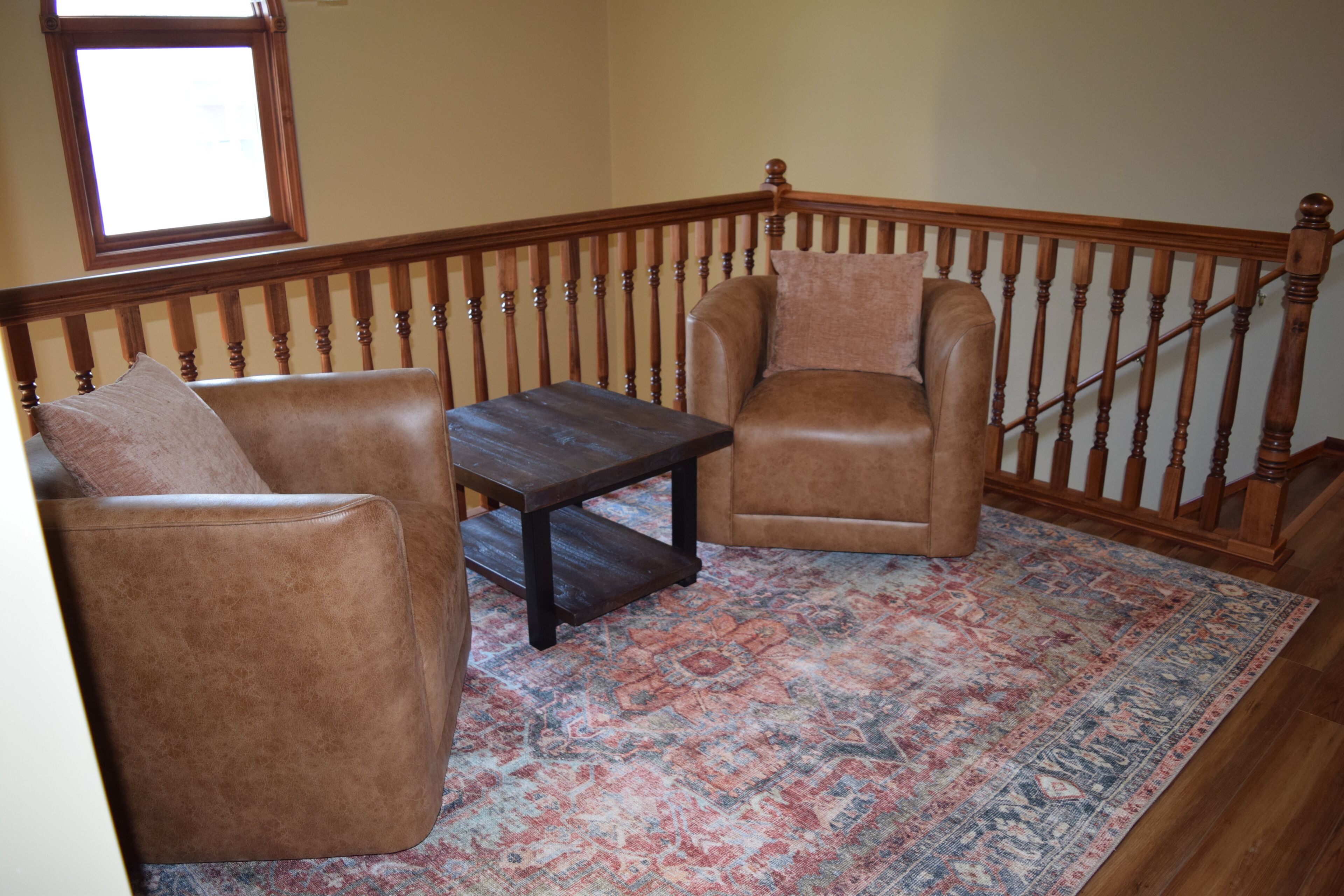 A corner room with a brown leather sofa, a matching armchair, a small wooden table, and a patterned rug.