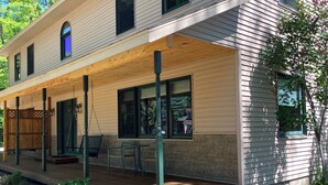 A two-story house with a covered porch, outdoor seating, and a stone foundation.