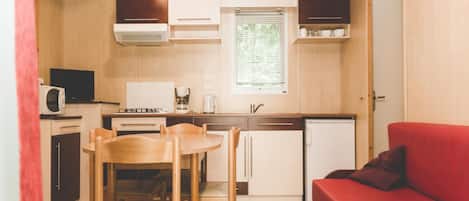 A compact kitchen with wooden cabinets, a microwave, a stove, and a sink. There is a dining area with a table and chairs, and a red sofa.