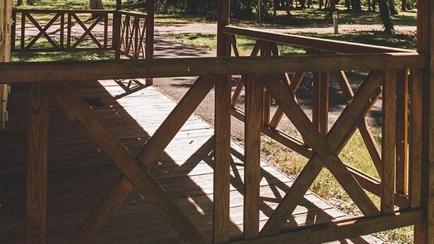 A covered pavilion with a wooden deck and railings, surrounded by trees.