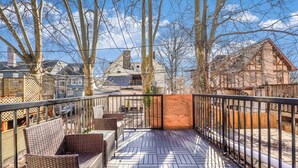En terrass med möbler av rotting, ett trästaket och hus i bakgrunden.