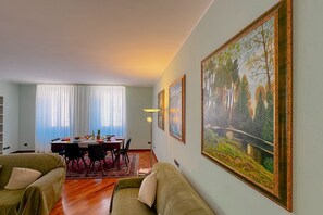A living room with a dining area, a sofa, and a painting on the wall.