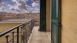 En balkon med udsigt til bygninger, klinkegulv og en grøn lukkedør.