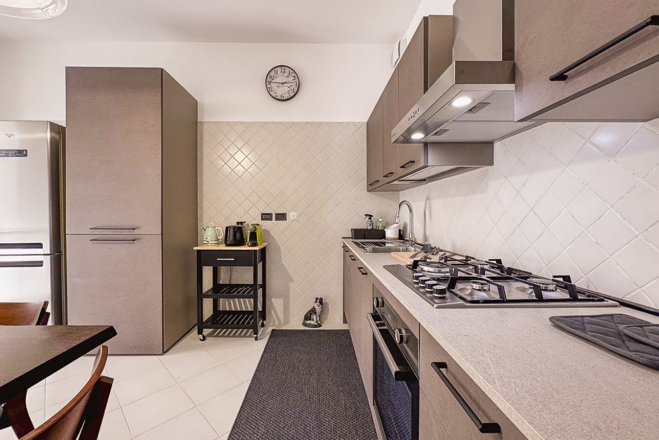 A modern kitchen with a gas stove, a refrigerator, and a clock on the wall.