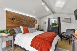 A bedroom with a wooden headboard, a bed with white and orange bedding, a nightstand with a lamp, a dresser, and a chair. - Direct Access to Brimstone Trails & River. Hot Tubs. Fire Pits. Pets (Huntsville)