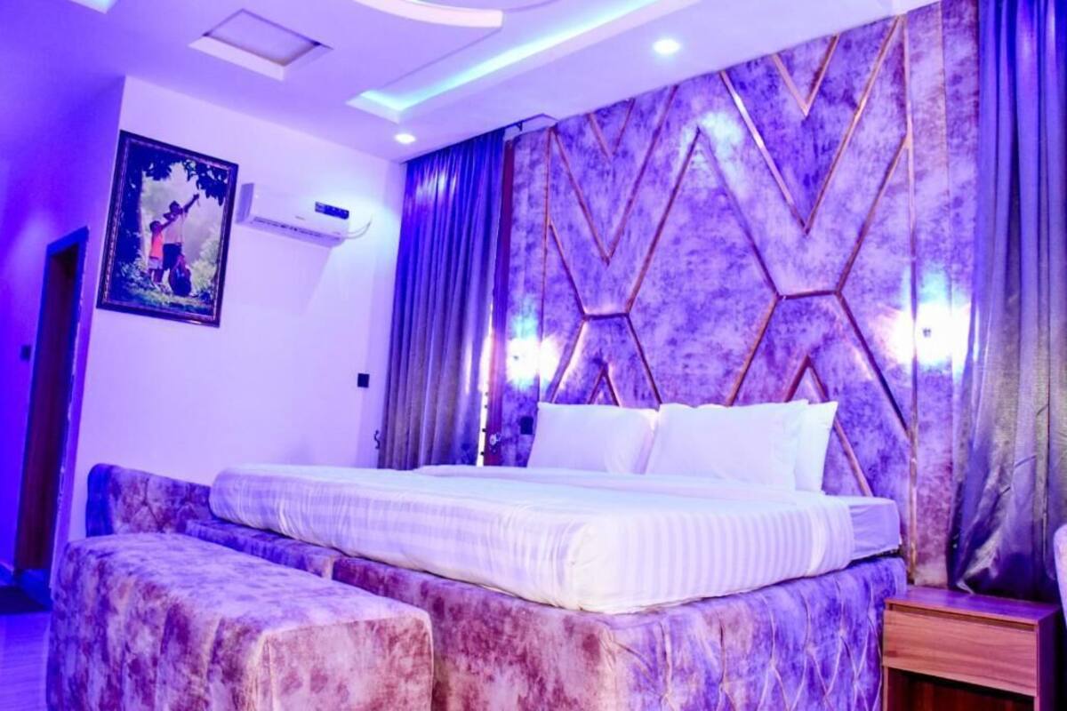 A modern bedroom with a bed, a headboard with geometric patterns, and a painting on the wall.