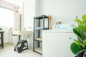 Zona de lavandería con lavadora, un lavamanos, un taburete y una estantería.