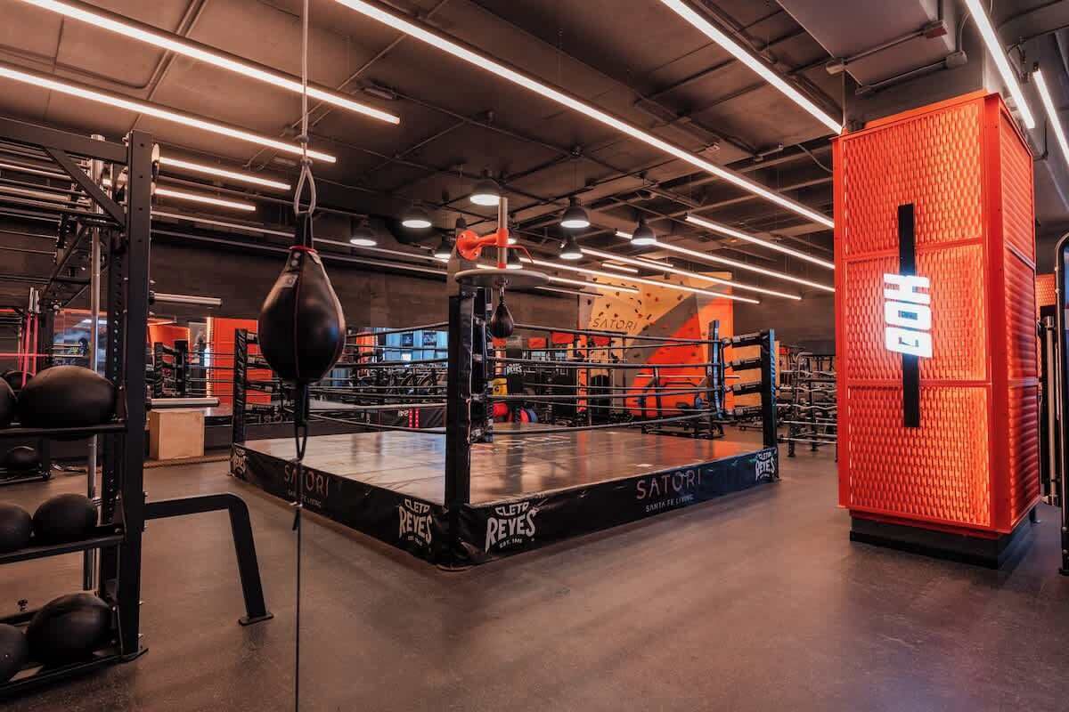 A boxing ring surrounded by gym equipment and a red storage unit.