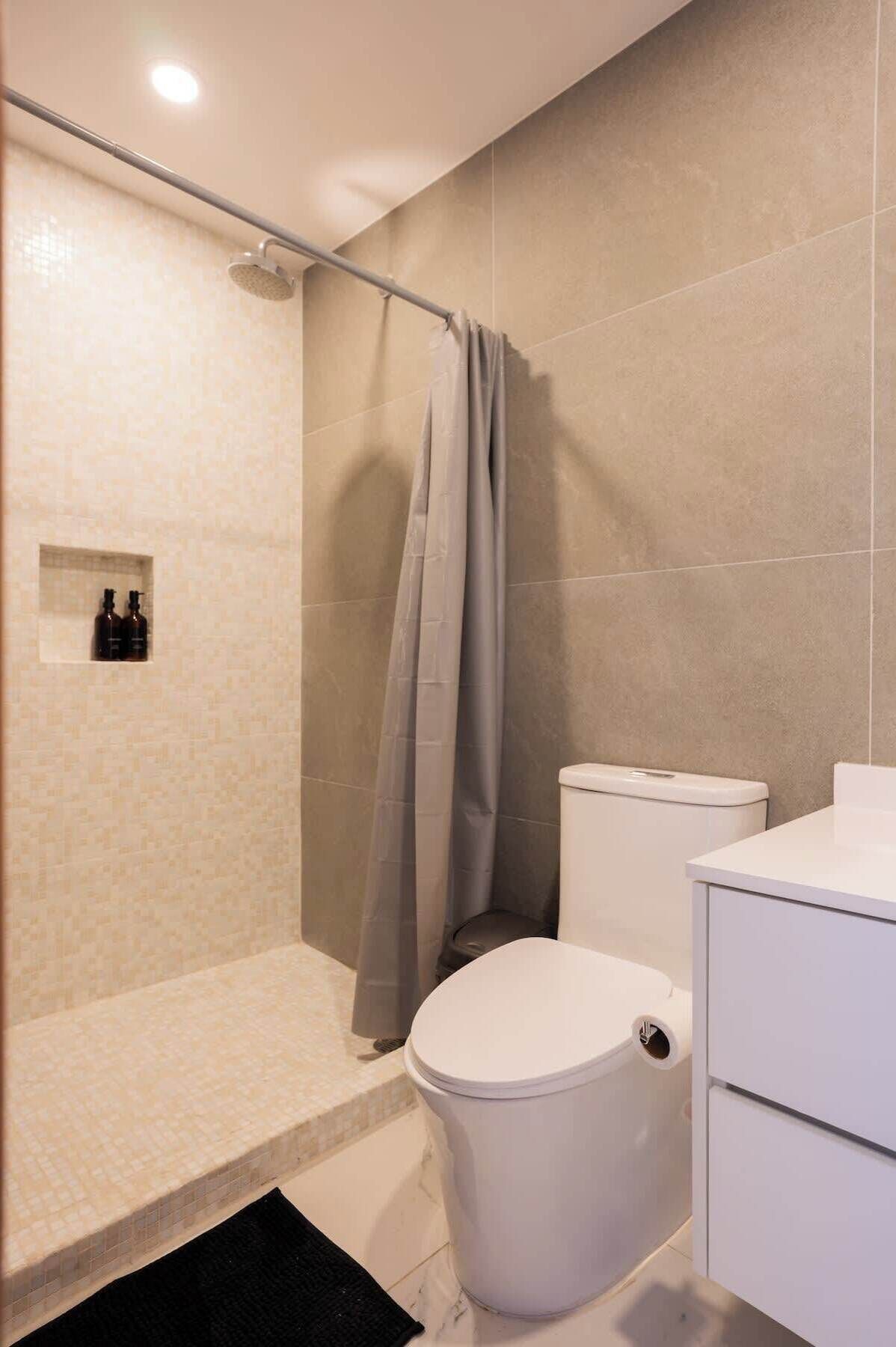 A bathroom with a shower, toilet, and a small shelf with bottles.