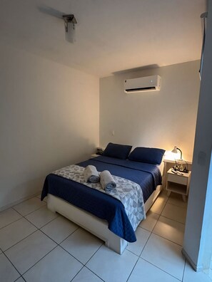 Ein Einzelbett mit gemustertem Bettbezug, ein Nachttisch mit Lampe und eine Klimaanlage an der Wand.