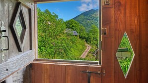 A wooden door with a triangular window revealing a lush green landscape with a winding road and a house. - Chalet La Grange d'Arlette with Mountain View (Sentein)