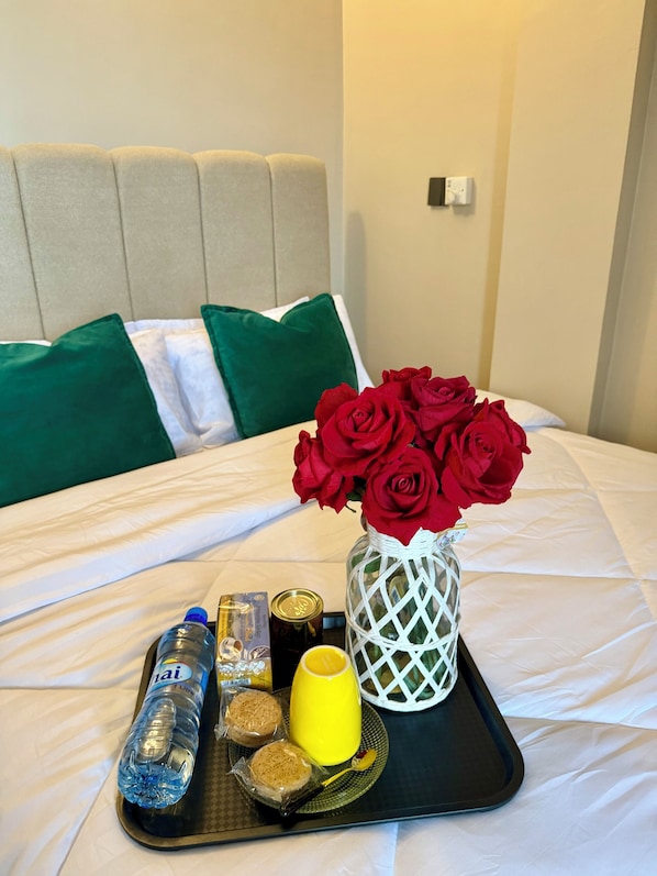 Un lit avec un plateau de petit-déjeuner, un vase de roses rouges et une bouteille d’eau.