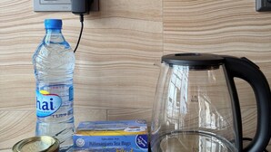A kitchen counter with a water bottle, a kettle, a box of tea bags, a can of coffee, and a packet of cookies.