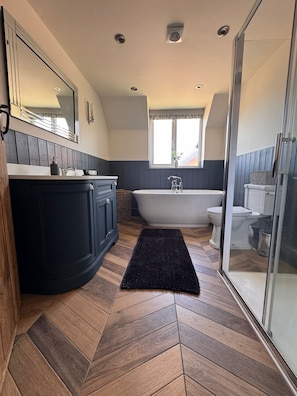 Un baño moderno con una bañera independiente, un espejo grande y un piso de madera con patrón de espiga.
