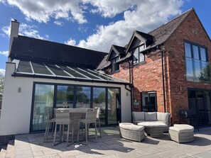A modern house with a glass conservatory, a brick extension, and outdoor furniture. - Cheshire escape. Golf course location. Hot Tub. 4 Ensuite bathrooms. sleeps 10. (Macclesfield)