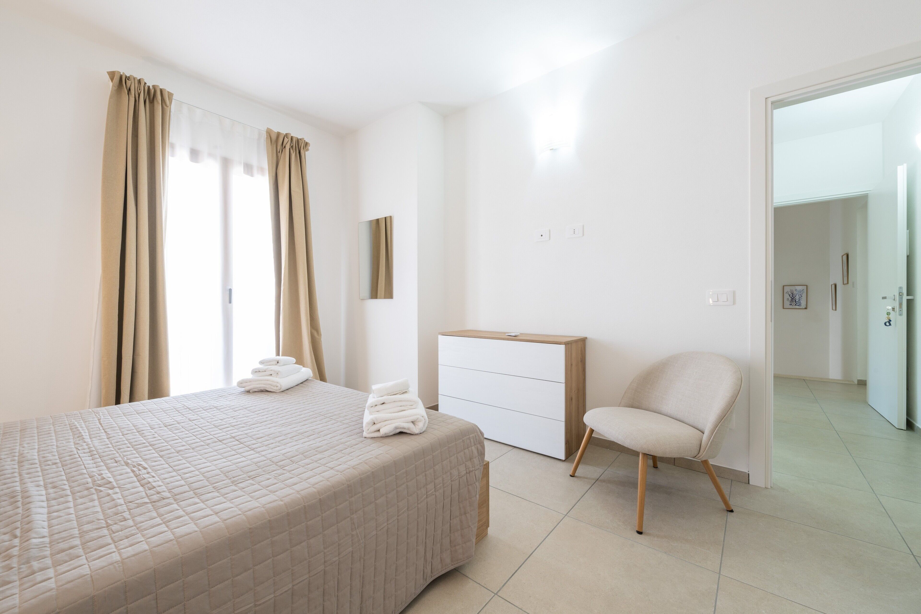 A bedroom with a bed, a chair, a dresser, and a door leading to another room.