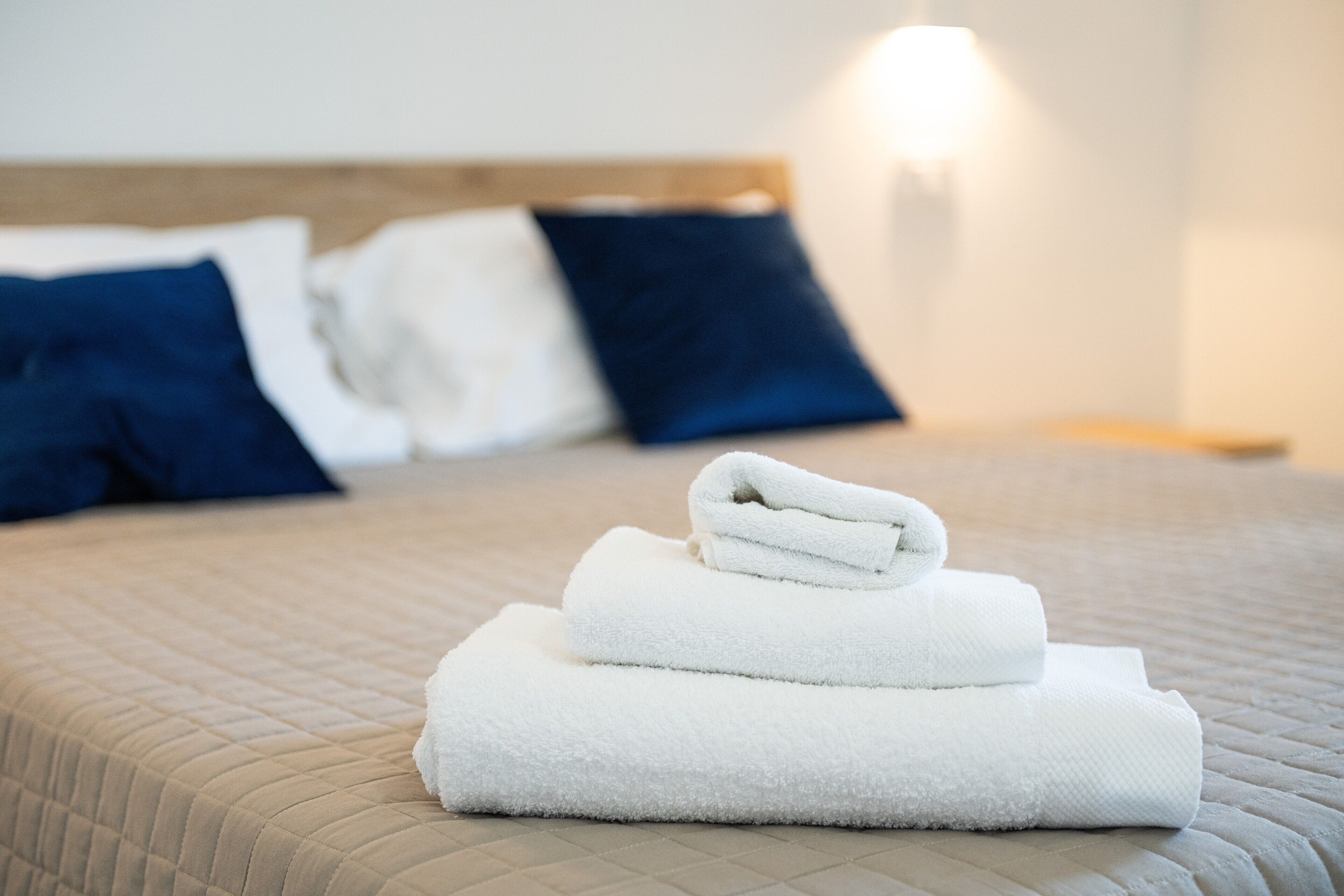 Un letto ben rifatto con un asciugamano bianco piegato sopra, una testiera in legno e una lampada da comodino.