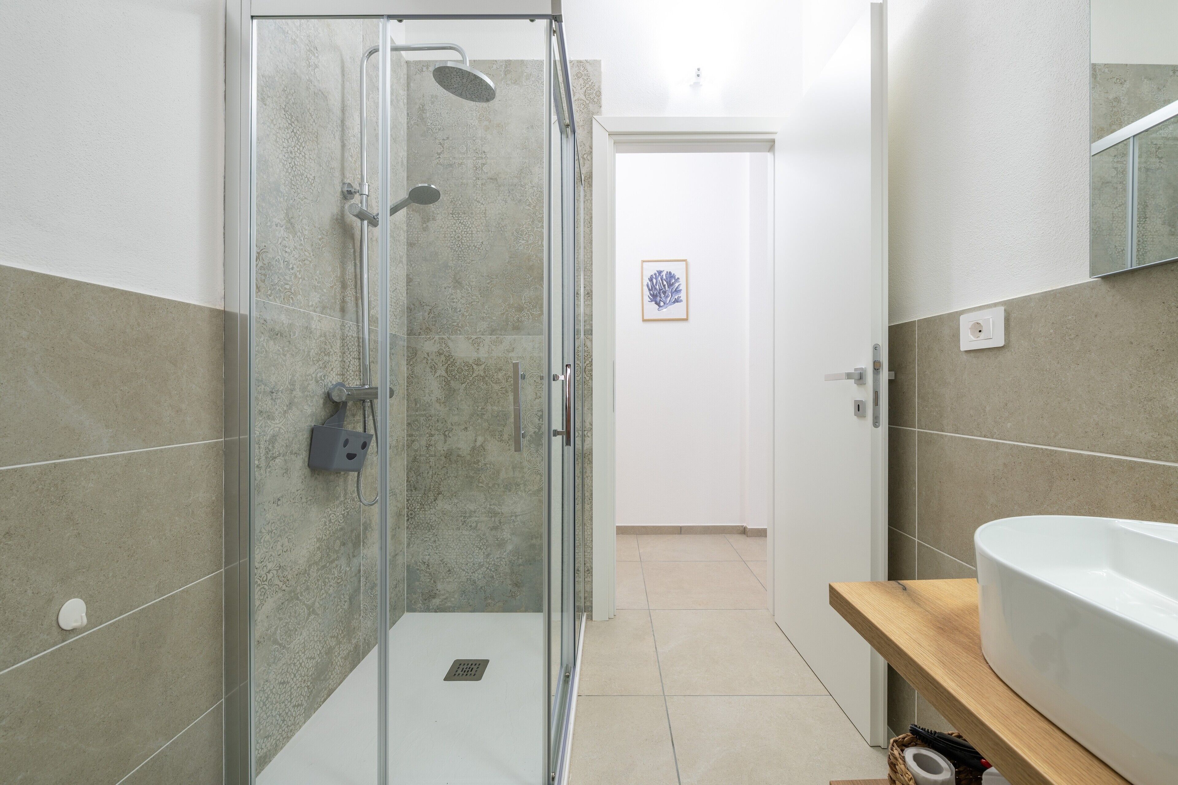 Un baño moderno con cabina de ducha de vidrio, lavabo blanco y tocador de madera.