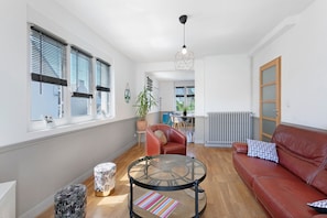 Una sala de estar moderna con una mesa de centro de vidrio, un sofá de cuero y un comedor al fondo.