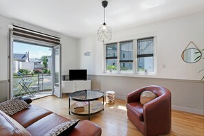 Una sala de estar moderna con sofá, sillón, mesa de centro de vidrio y un televisor sobre un mueble.
