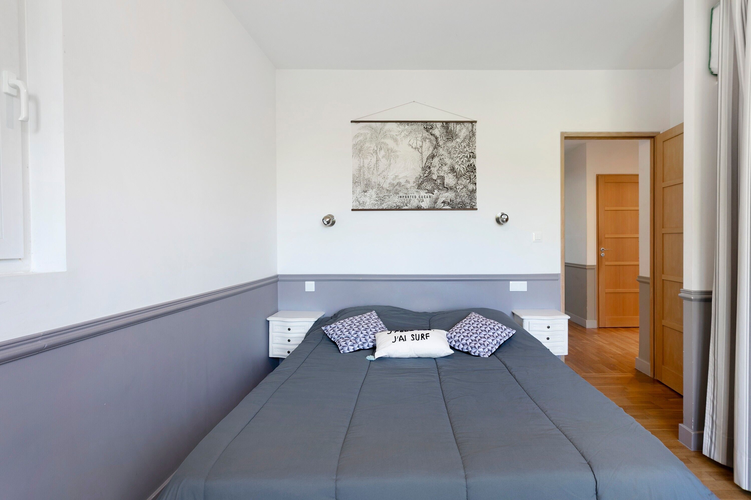 A bedroom with a bed, a nightstand, a wall-mounted artwork, and a door leading to another room.