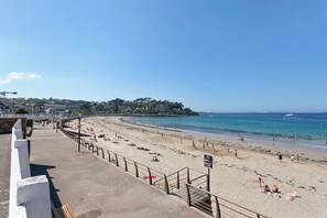 Ein Strand mit einer Uferpromenade, Blick aufs Meer und Gebäuden im Hintergrund.