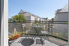 Varanda com mesa, cadeiras, um vaso de planta e vista para prédios vizinhos.