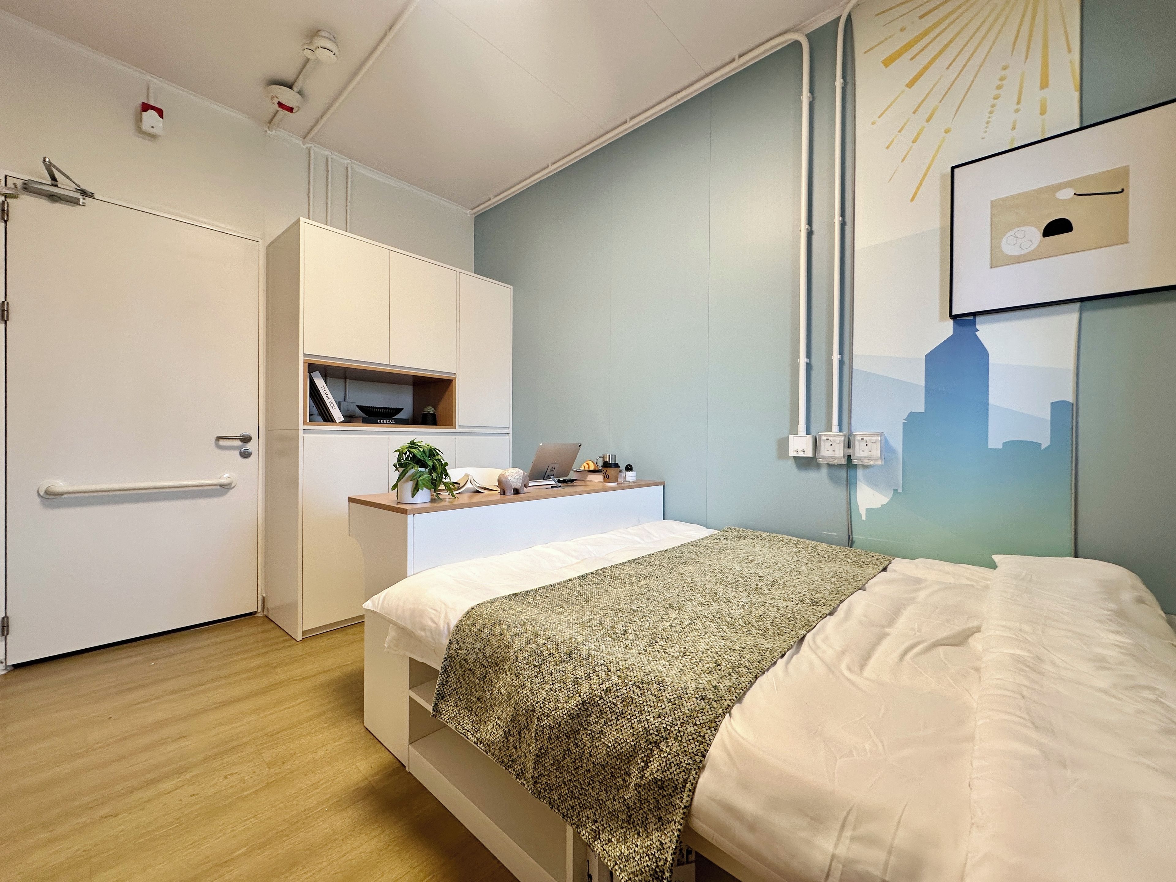 A modern bedroom with a bed, bedside table, and a cityscape artwork on the wall.