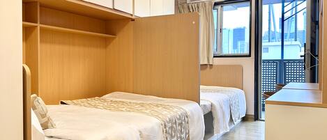 A compact room with two beds, a wardrobe, and a window with a view of buildings.