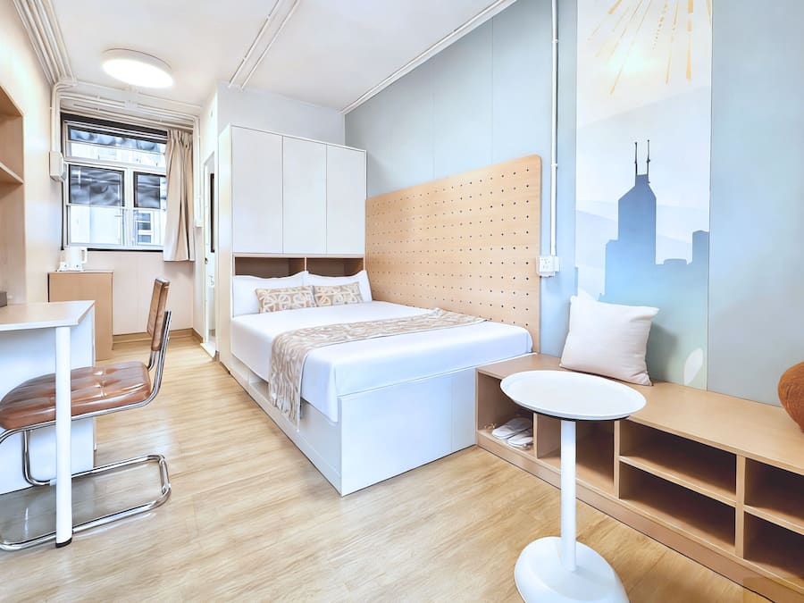 A modern hotel room with a bed, a desk, a chair, a round table, and a cityscape mural.